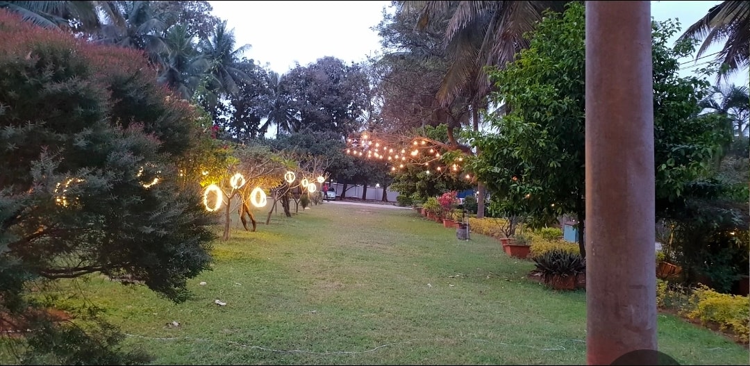 Sprawling resort lawns at Kalathur Gardens with glowing ring lights and mature trees at dusk